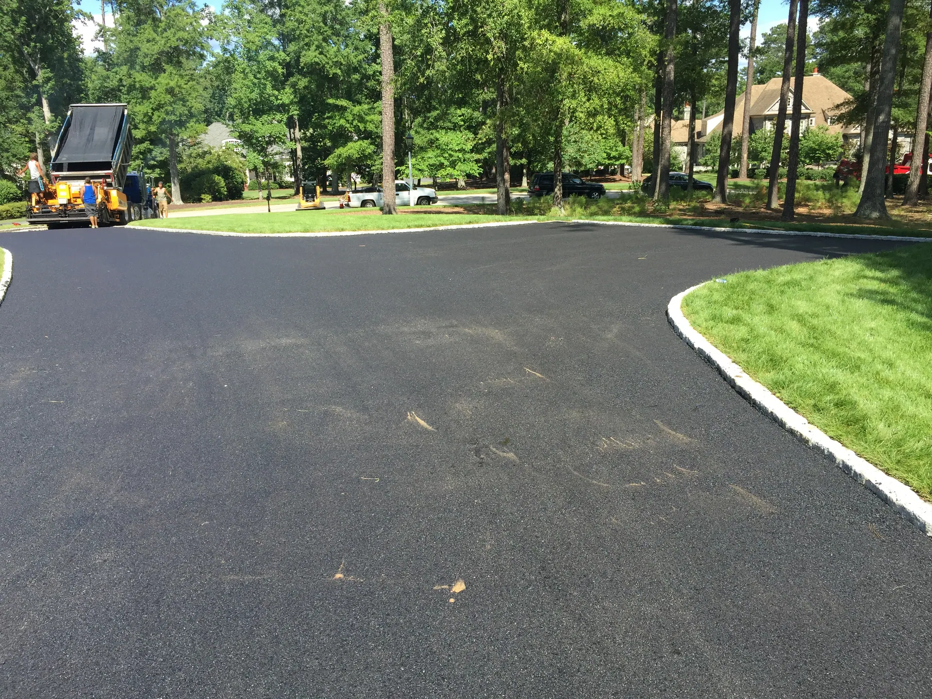 Crew and paver laying hot mix on an estate driveway with cobblestone borders
